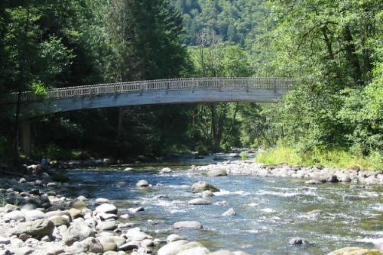 Photo shows a bridge crossing the Wild and Scenic Salmon River in a mountainous, forested environment with river rocks in the foreground.