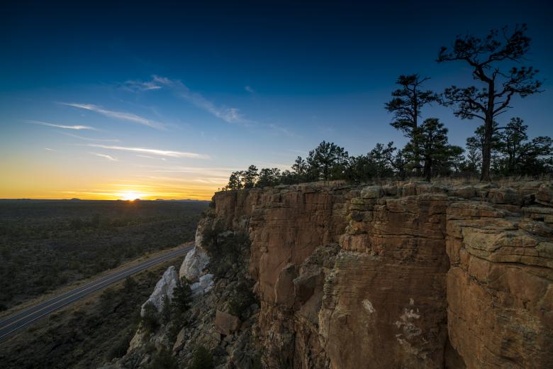Looking at a cliff in Malpais NCA with the sun setting and sky turning darker blue beyond.