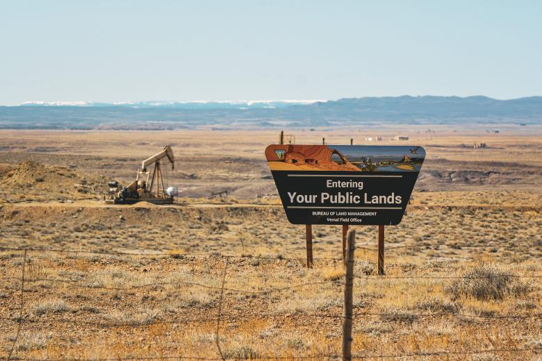 Welcome to your public lands sign in foreground with a pump jack in the background 