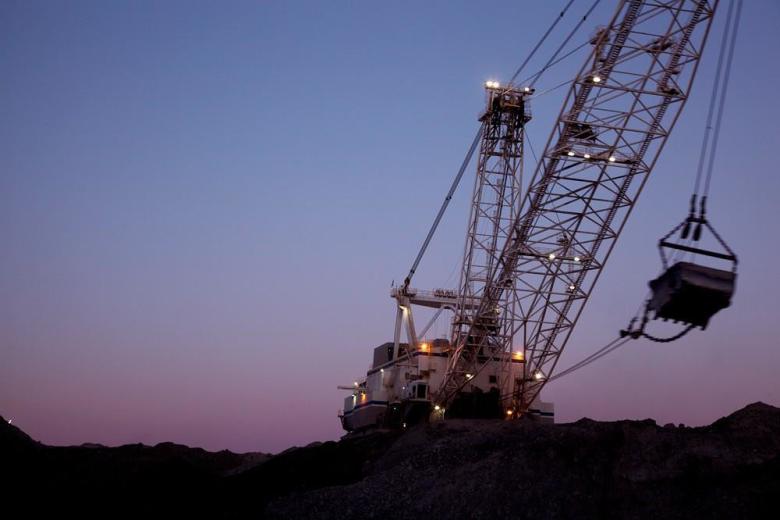 A dragline is silhouetted against a purple and blue sky at an open pit coal mine.