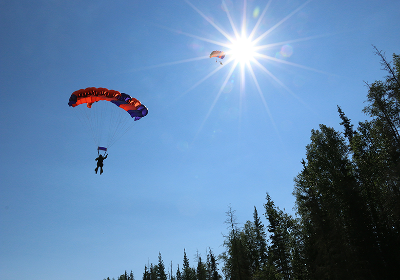 Two smokejumpers decend to the ground under blue skies and a shining sun.