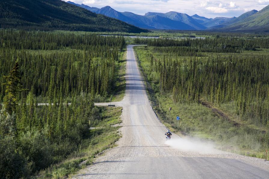 Motorcycle in the distance on gravel road surrounded by spruce forest
