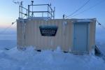 A shipping container with a trapezoid sign that reads "Bureau of Land Management Alaska Kaktovik Air Quality Monitoring Station."