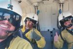 Three wildland firefighters in a helicopter smiling and giving thumbs up to the camera.