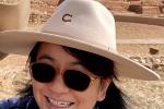 Hebin Lin, who is wearing a brimmed hat and sunglasses, smiles in front of Pecos National Park in New Mexico.