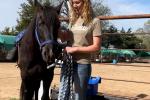 A woman smiles as she stands next to a black horse. 