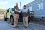 A Native American man poses shaking hands with a Caucasian man next to a green yellow truck