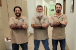 Three men pose together in an office hallway.