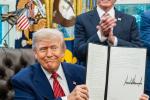 President Trump sits at his desk and holds up one of the energy executive orders he signed with Secretary of the Interior Burgum standing behind him clapping in the oval office.
