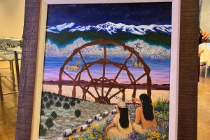 Vividly painted art showing two long haired figures sitting in wildflowers looking out at a layered distance with wagons disappearing into mountains.